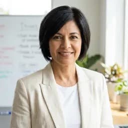Smiling professional woman with short black hair wearing a cream blazer in an office.